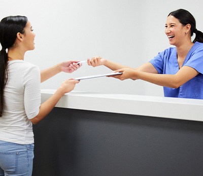 Smiling dental assistant handing patient form