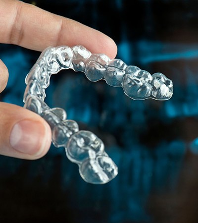 person holding a clear aligner in front of a dental X-ray 
