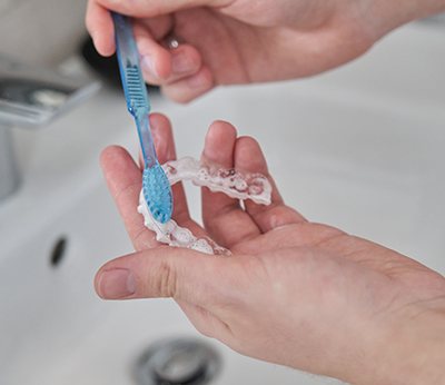 Patient using toothbrush to clean aligner
