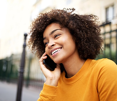 Woman in orange shirt smiling while talking on phone