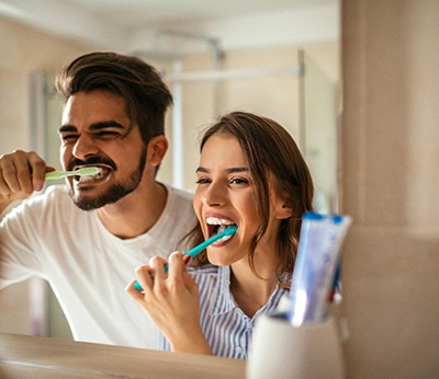 Man and woman brushing teeth together at bathroom sink